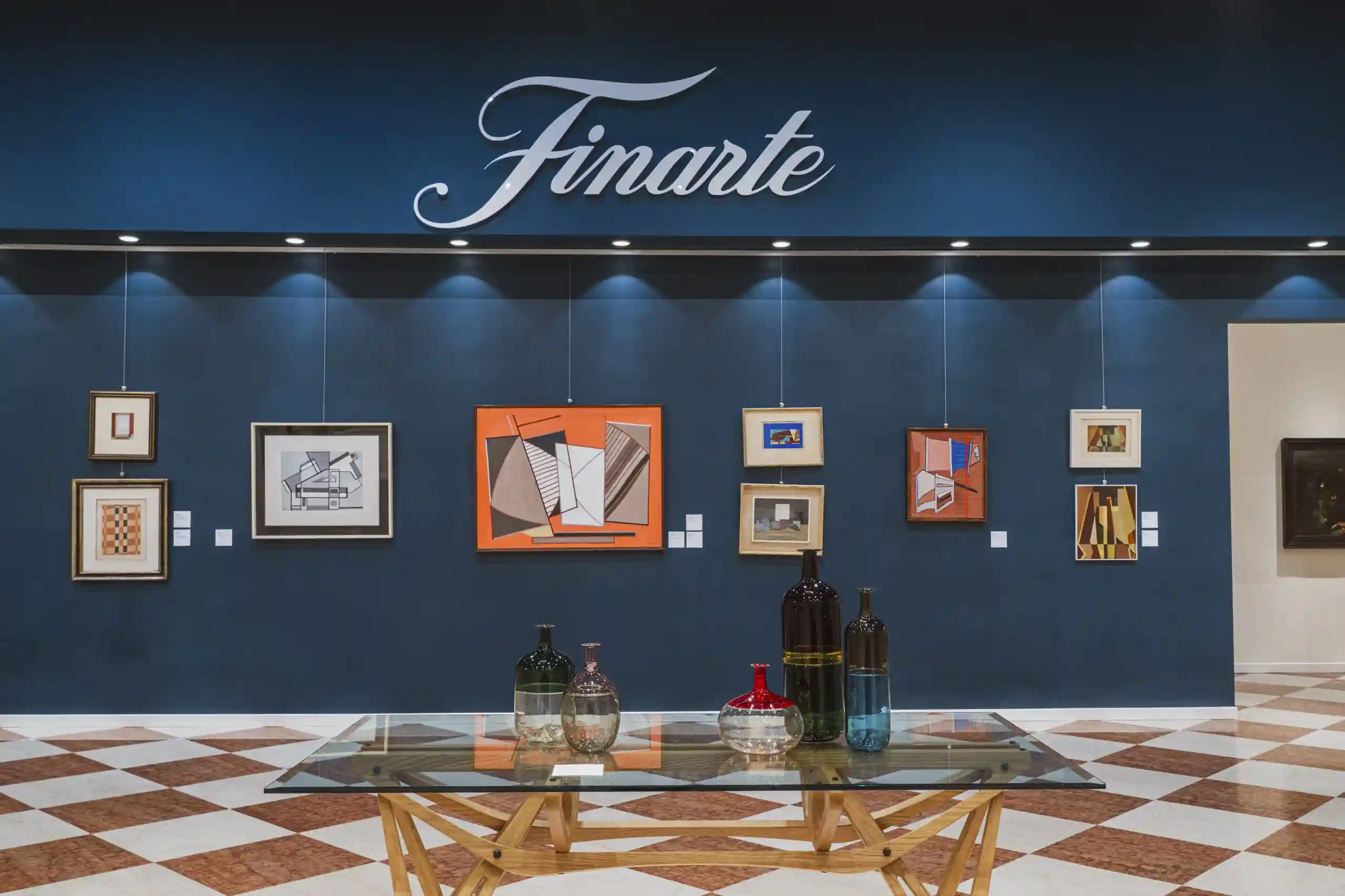 Opere d'arte astratta e vasi di vetro su un tavolo di vetro, con logo "Finarte" in alto.