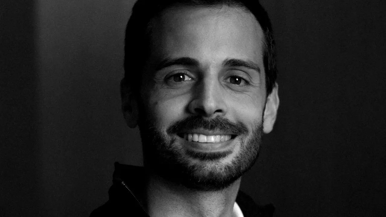 Uomo sorridente con barba e baffi, in bianco e nero.