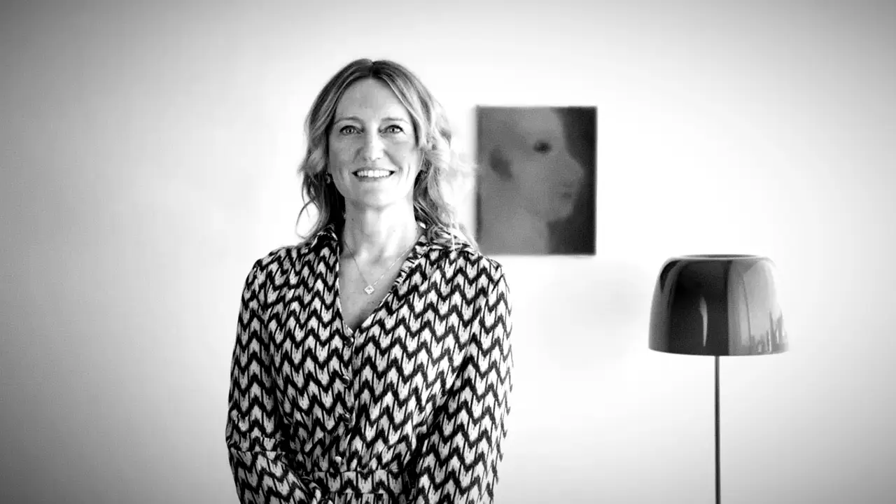 Donna sorridente in camicia a fantasia, quadro astratto e lampada da terra.