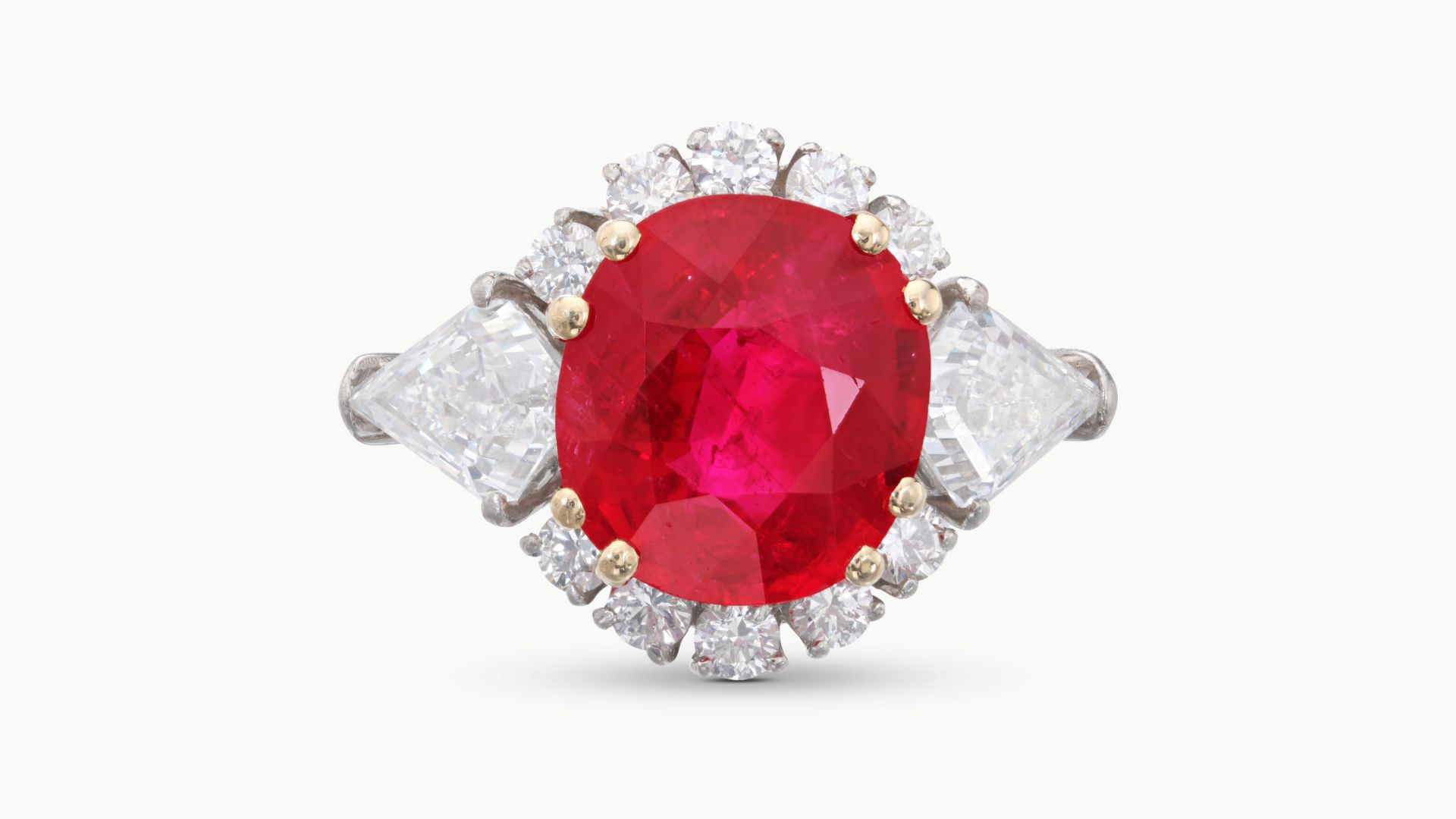 Anello con rubino centrale, diamanti laterali a goccia e contorno di diamanti rotondi.
