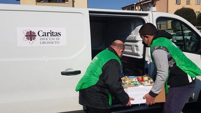 Volontari Caritas caricano cibo in un furgone bianco.
