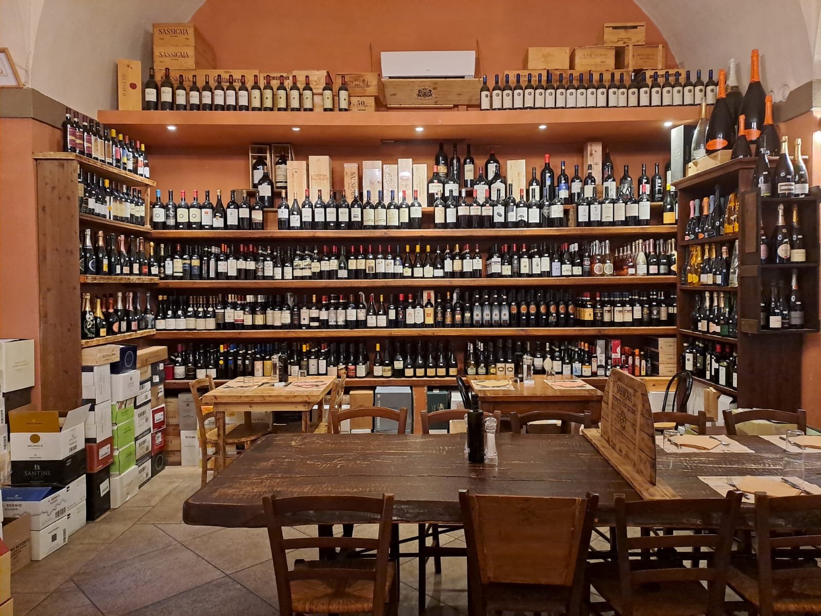 Scaffali pieni di bottiglie di vino, tavoli in legno e sedie in un negozio.