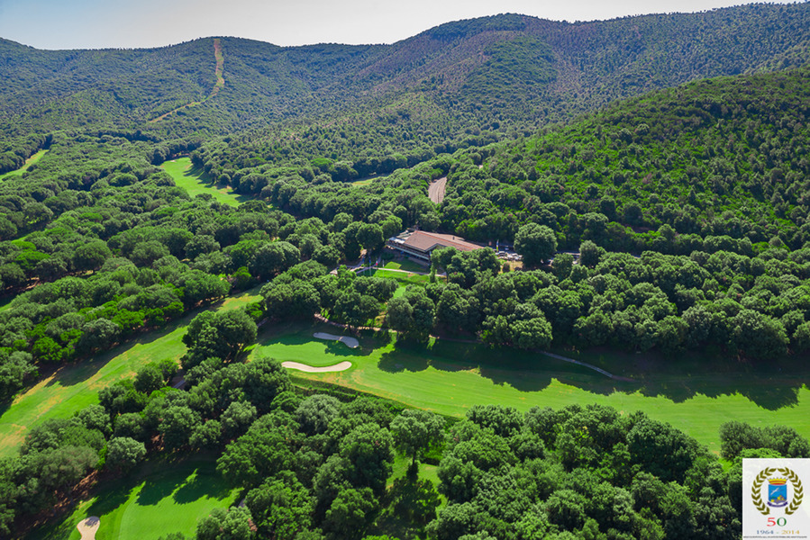 Campo da golf immerso in una lussureggiante foresta verde con un edificio centrale e colline sullo sfondo.