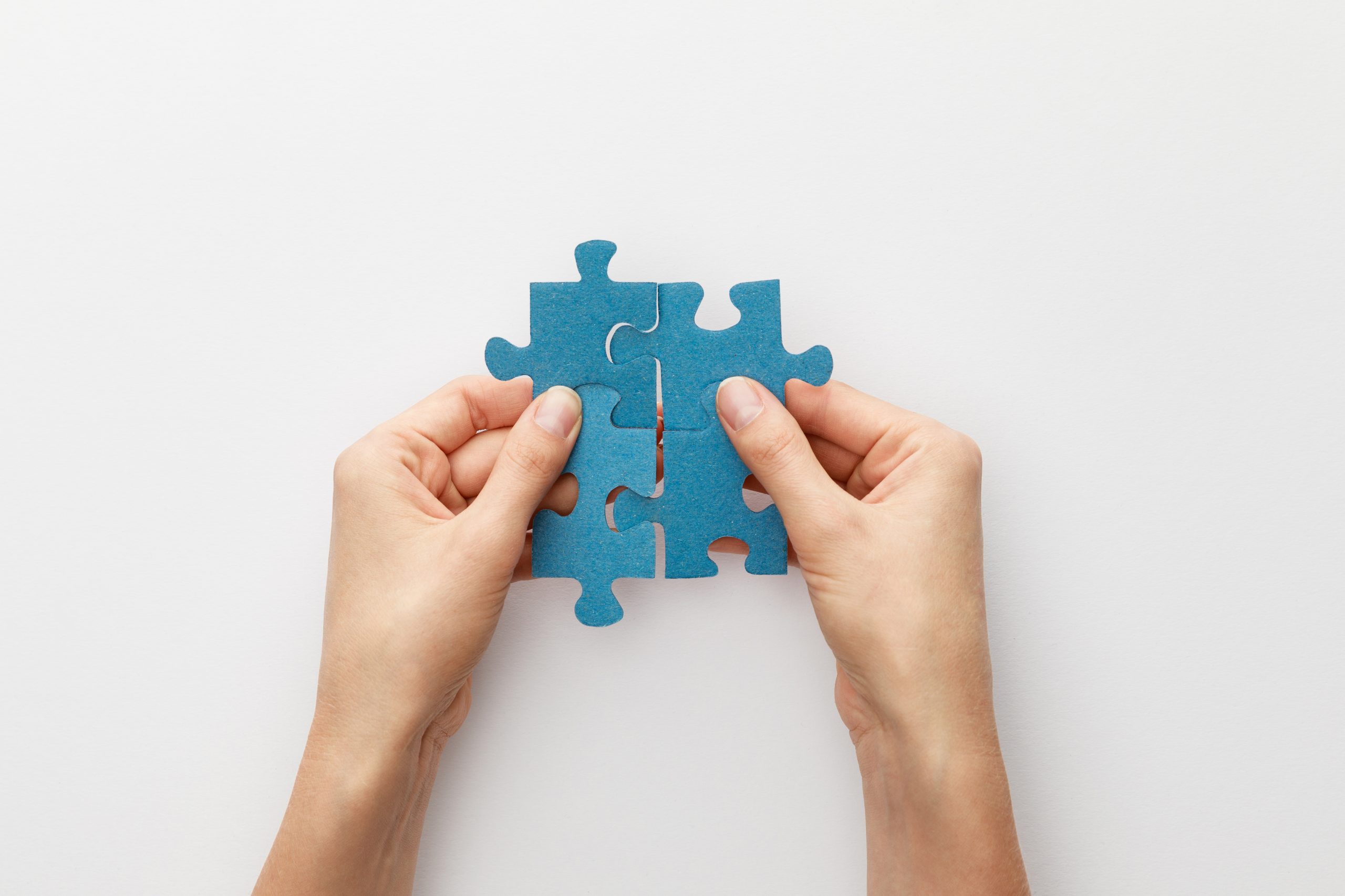 Mani che assemblano pezzi di puzzle blu su sfondo bianco.