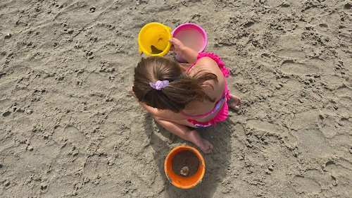 Bambina con secchielli colorati gioca sulla sabbia umida.