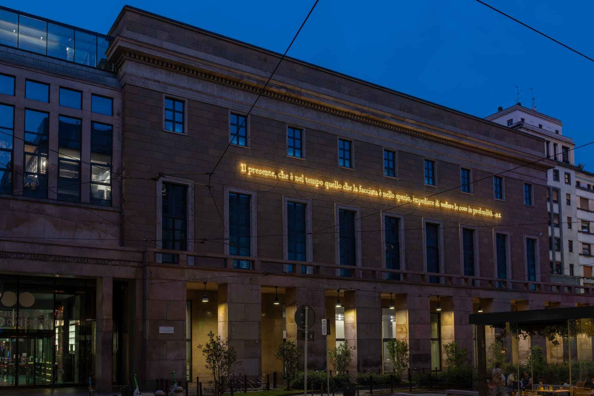 Scritta al neon su edificio storico, con finestre blu e cielo serale.