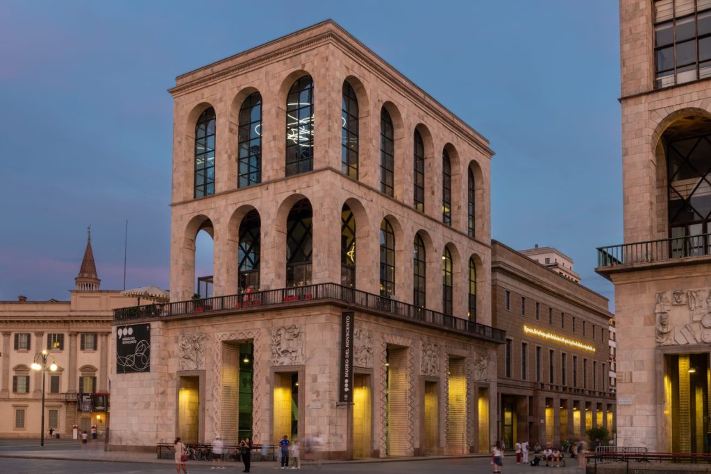 Edificio storico con archi, finestre alte e sculture. Museo del Novecento visibile.