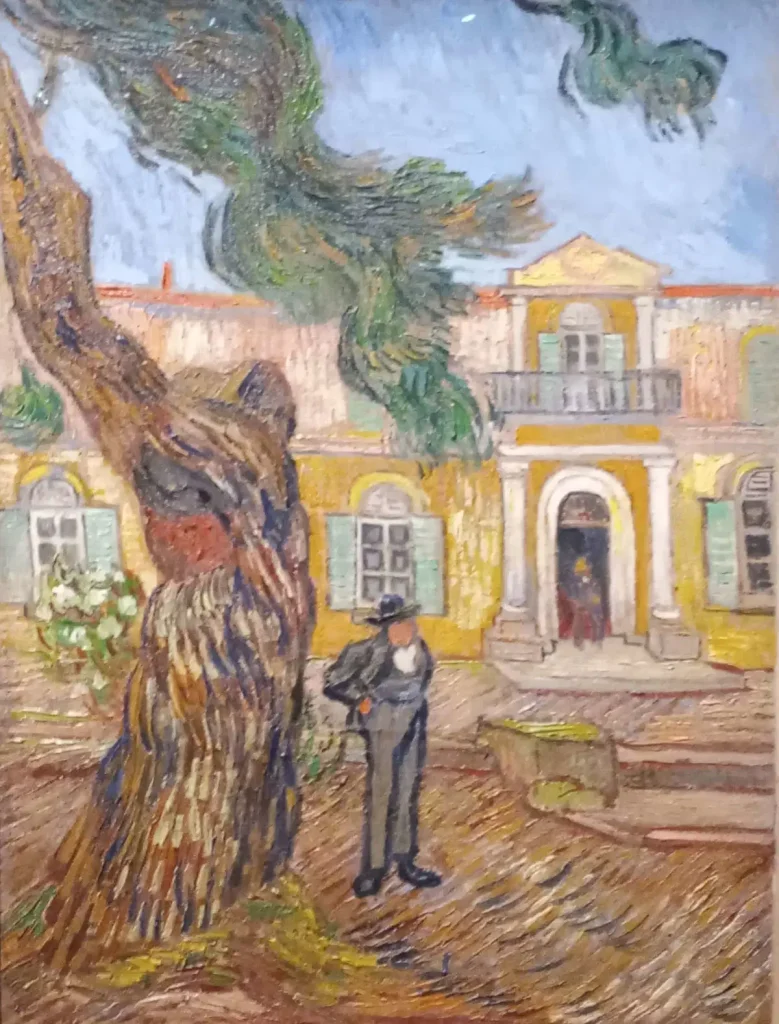 Uomo con cappello davanti a una casa gialla con un grande albero e vegetazione.