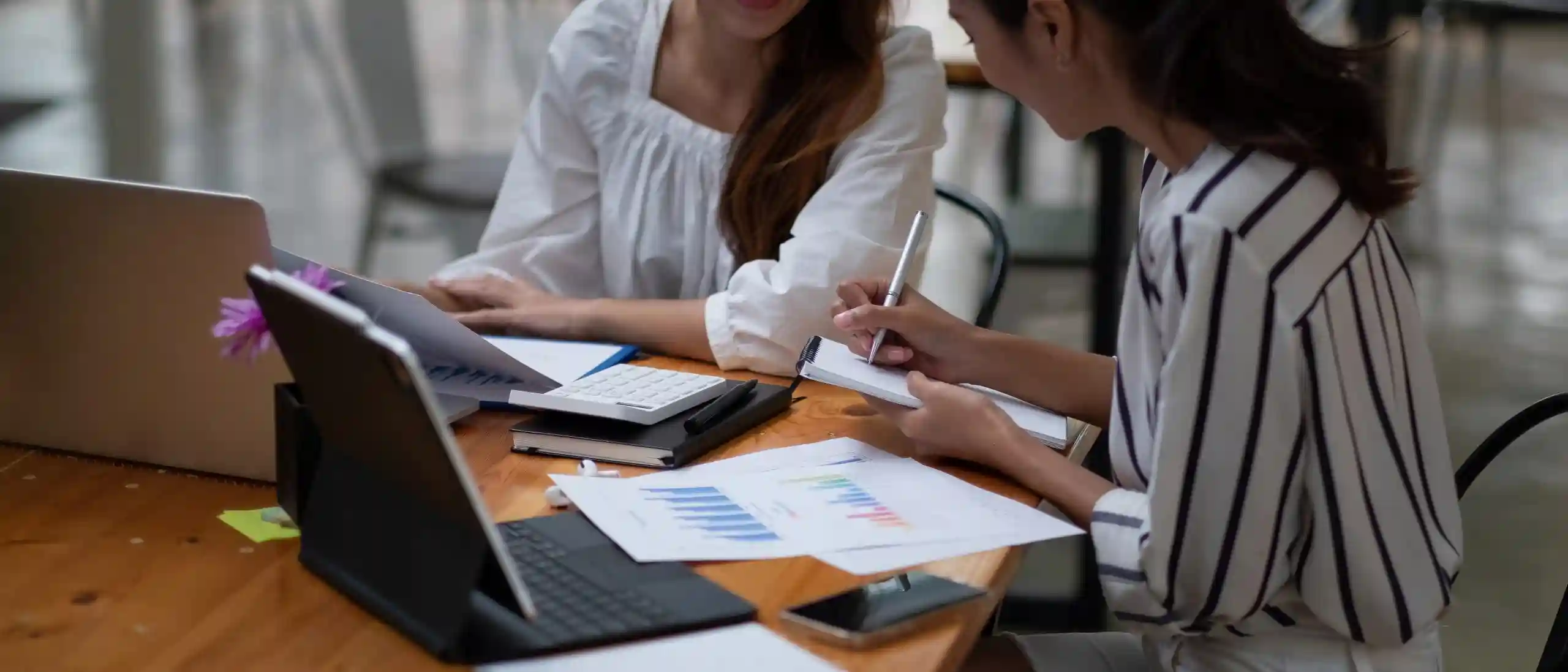 Due donne lavorano a un tavolo con laptop, grafici e calcolatrice.