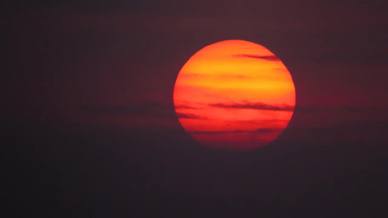 Sole rosso acceso con nuvole sottili contro un cielo scuro.
