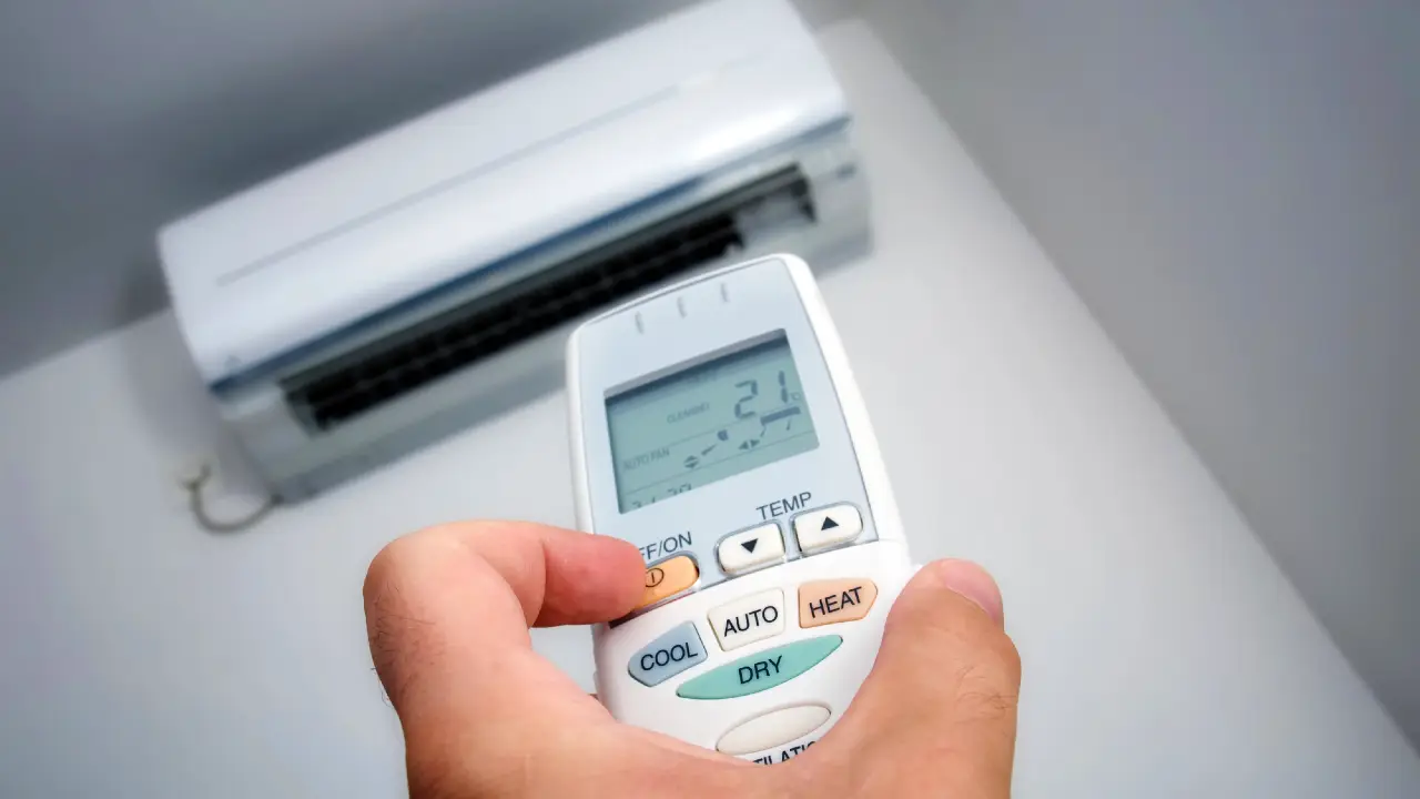 Mano che tiene il telecomando di un condizionatore d'aria impostato a 21 gradi.
