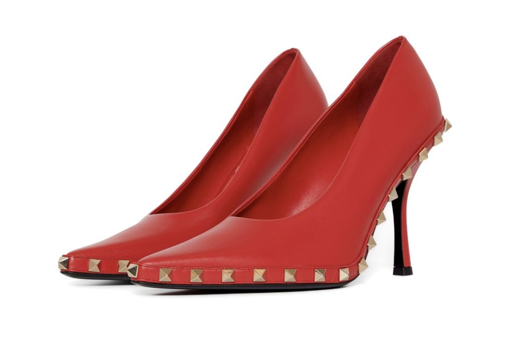 Scarpe rosse con tacco alto, decorate con borchie dorate lungo il bordo e sul tacco.