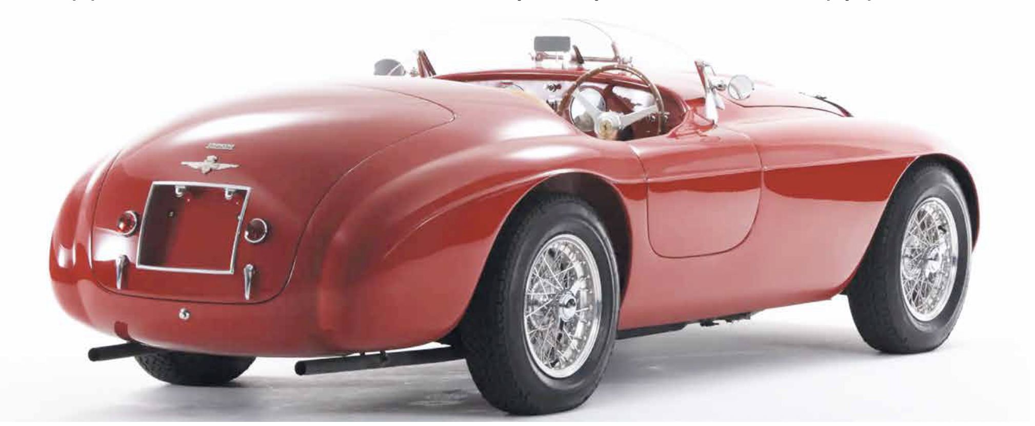 Auto sportiva rossa d'epoca con ruote a raggi e volante in legno.