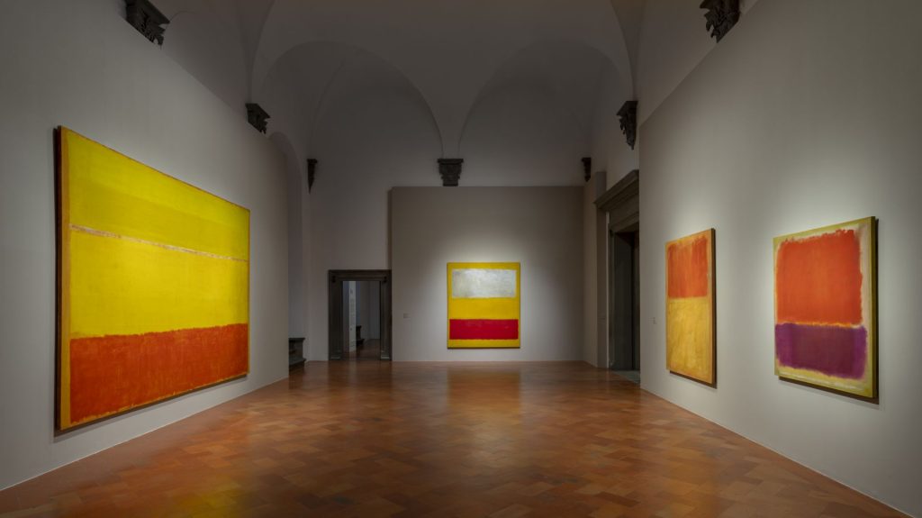 Opere astratte con blocchi di colore giallo, rosso, arancione e viola in una galleria.