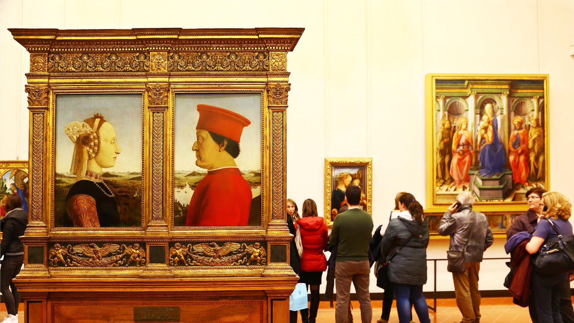 Coppia di ritratti rinascimentali dorati, visitatori osservano opere d'arte in un museo.
