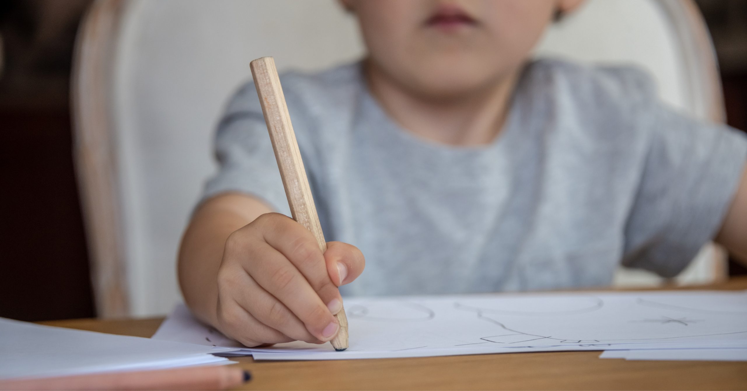 Bambino con la mano che tiene una matita di legno, disegna su un foglio.