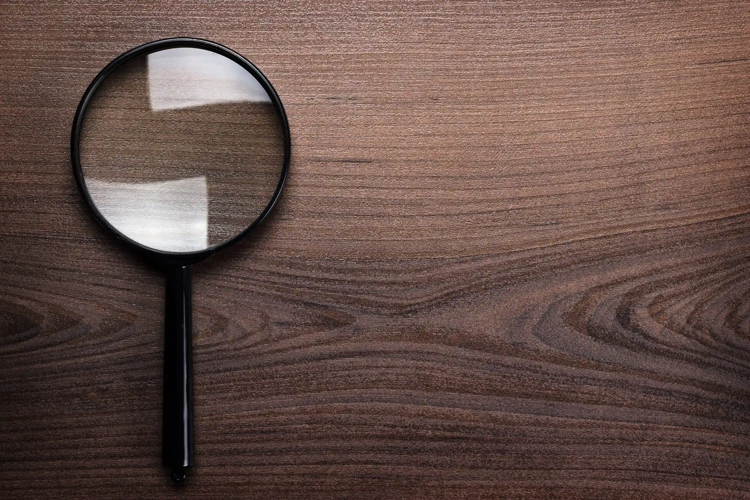 Lente d'ingrandimento nera su sfondo di legno scuro con riflessi luminosi.