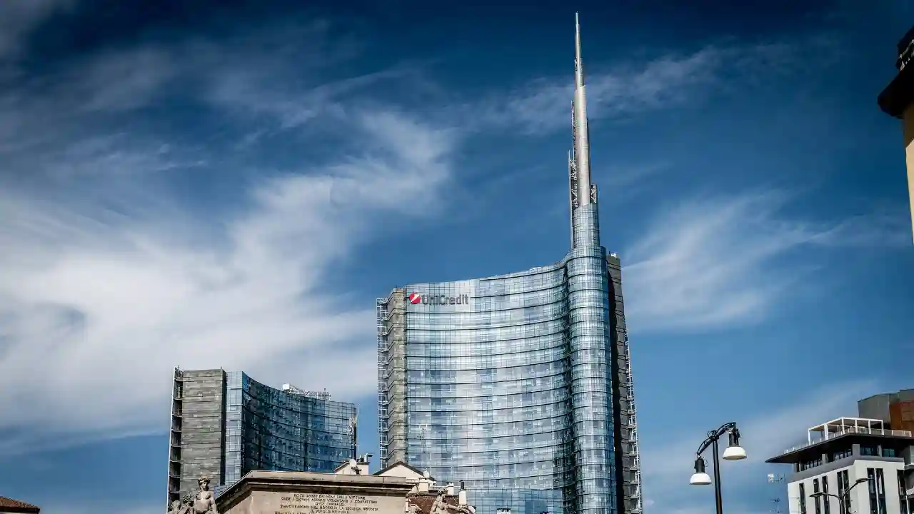 Grattacielo moderno con logo UniCredit, sotto un cielo blu con nuvole bianche.