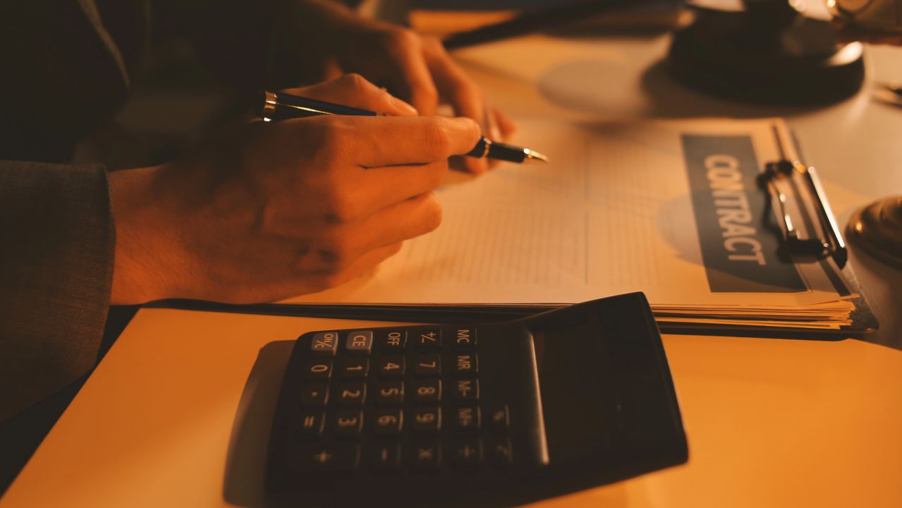 Firma di un contratto di mutuo con calcolatrice in primo piano per il calcolo dei tassi mutui 2026.