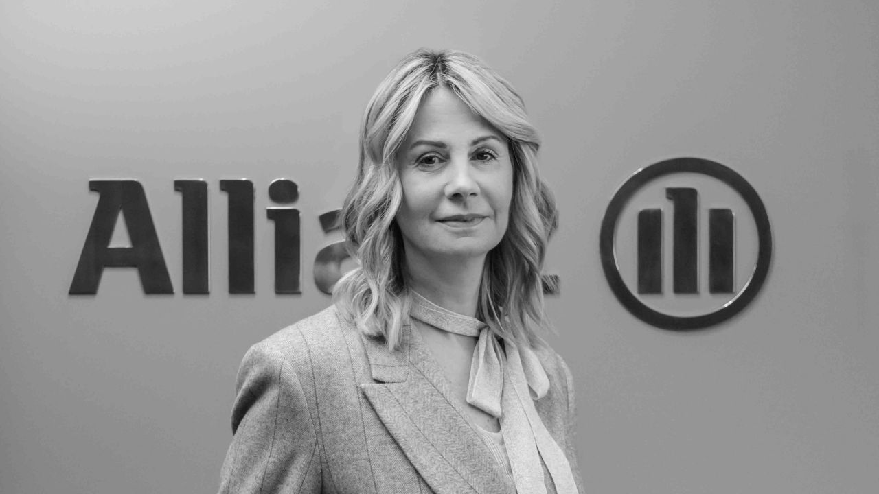 Donna con blazer e sciarpa, con logo Allianz sullo sfondo.