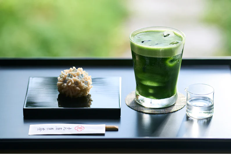 Dolce giapponese, tè verde ghiacciato e bicchierino d'acqua su vassoio nero.