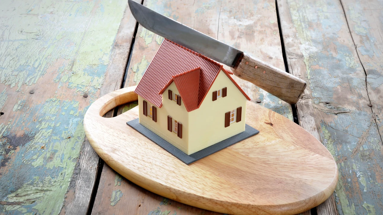 Casa in miniatura su tagliere di legno, con coltello sopra, che riporta alla mente la casa in comproprietà e i possibili litigi.