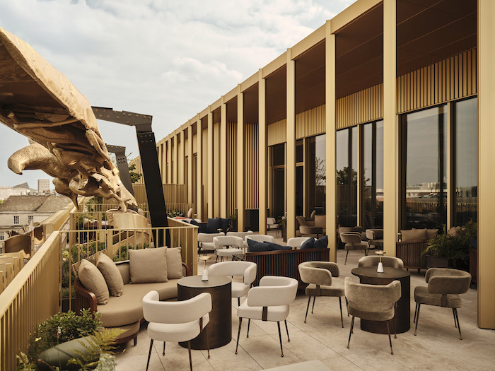 Terrazza con scultura dorata, arredi moderni e vista sulla città.