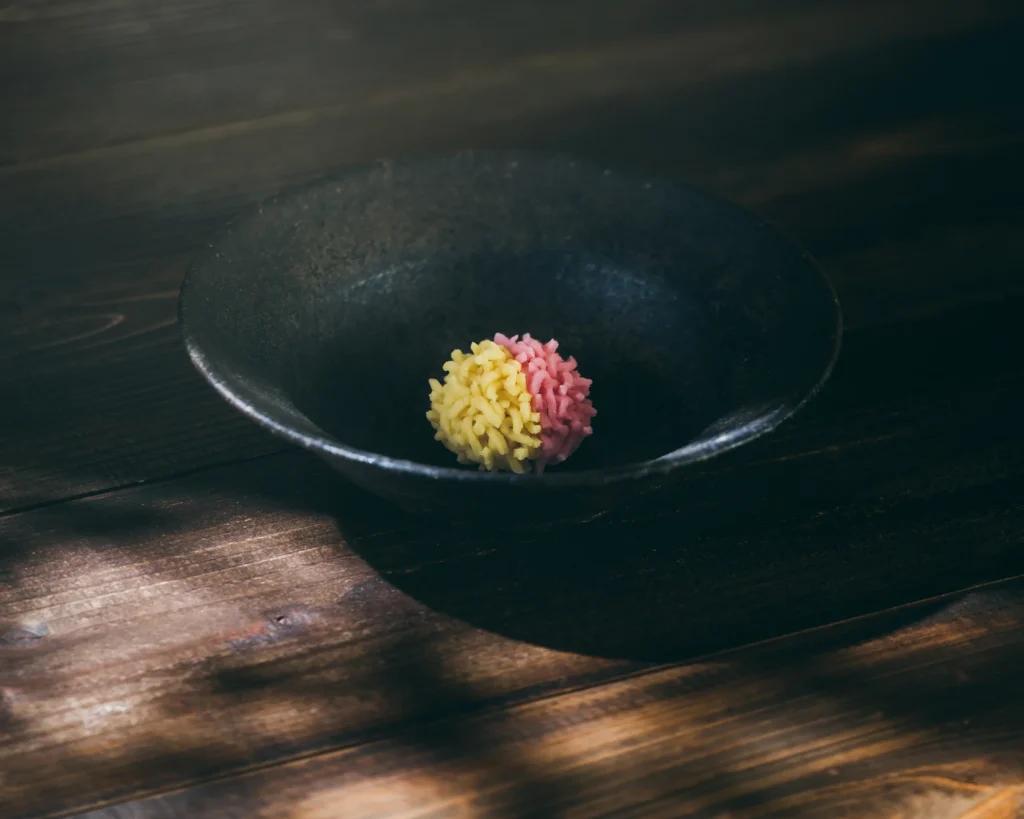 Dolce sferico giallo e rosa in una ciotola nera su un tavolo di legno scuro.