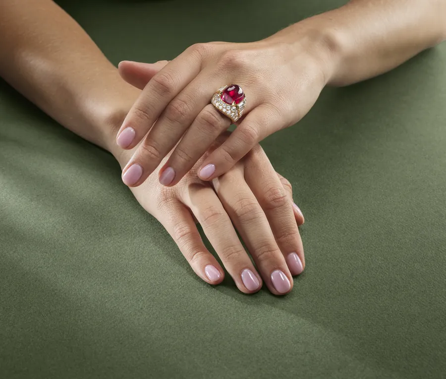Mani con anello con rubino e diamanti su sfondo verde.
