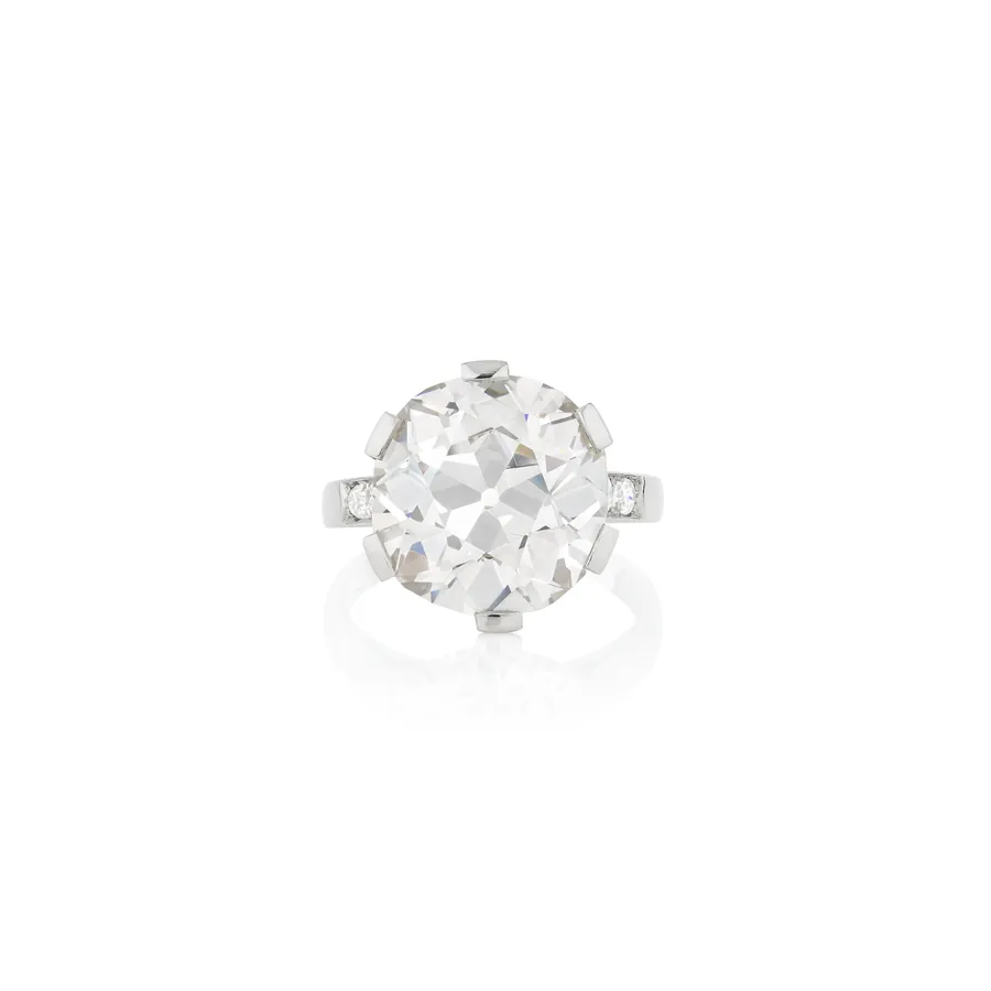 Anello con grande diamante rotondo sfaccettato, incastonato in metallo bianco con piccoli diamanti laterali.