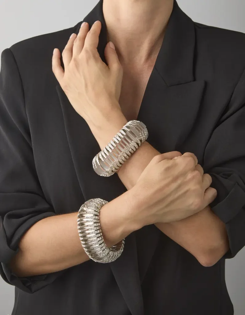 Bracciali rigidi argentati con dettagli a coste e pietre scintillanti su braccia incrociate.