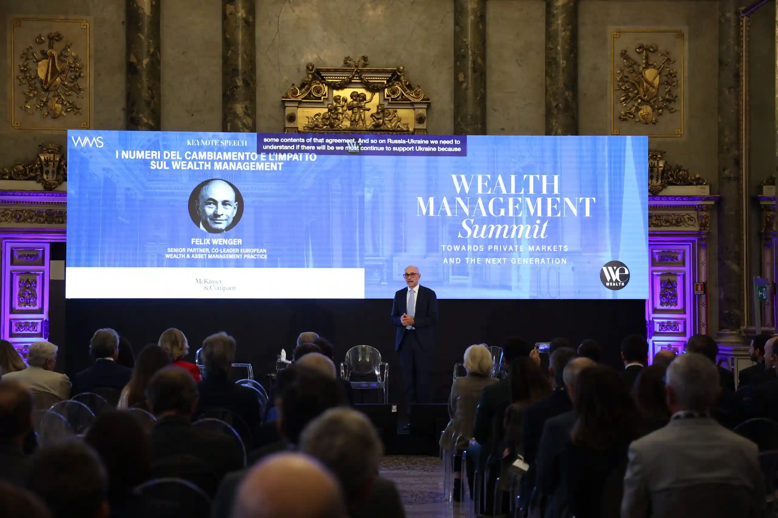 Uomo in abito parla a un pubblico durante un evento di gestione patrimoniale.