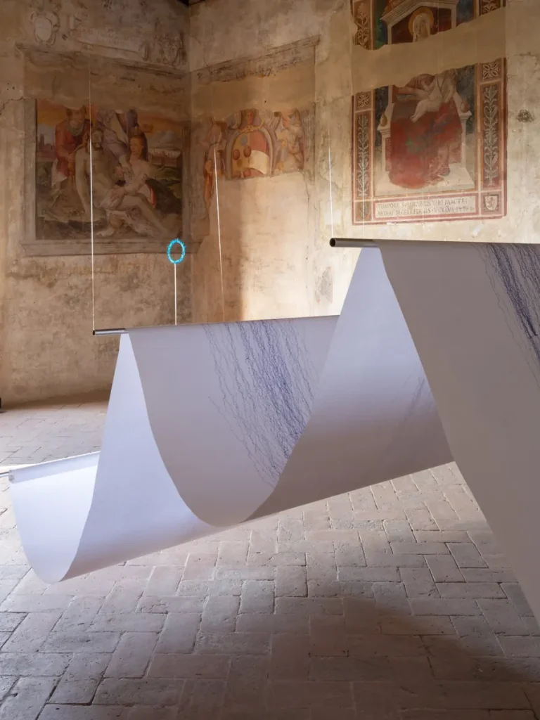 Rotolo di carta bianco con disegni a matita blu, appeso in una stanza con affreschi.