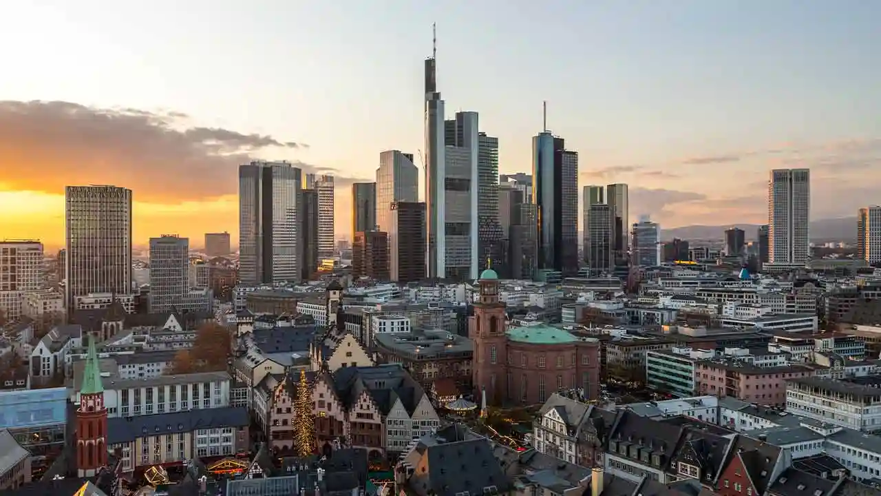 Grattacieli moderni e edifici storici sotto un cielo al tramonto con nuvole arancioni.