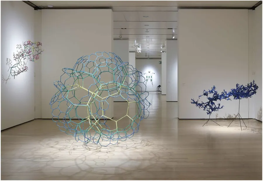 Sculture geometriche e ramificate in una galleria d'arte bianca con luci soffuse.