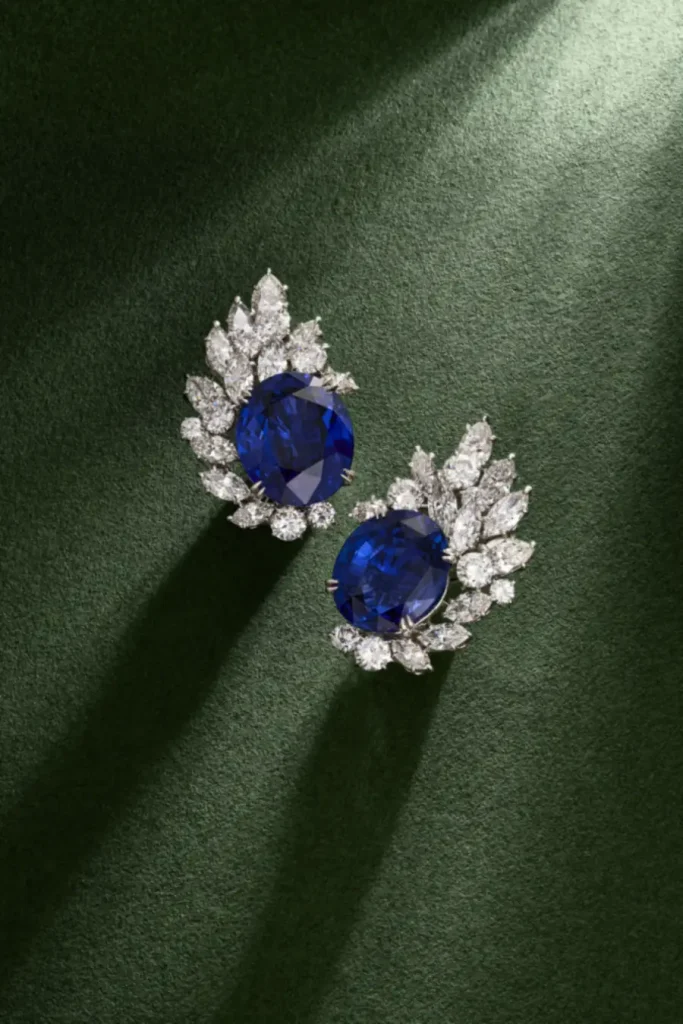 Orecchini con zaffiri blu ovali e diamanti bianchi a forma di foglia su sfondo verde.