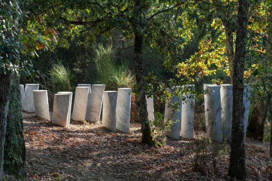 Colonne di marmo disposte in cerchio in un bosco autunnale illuminato dal sole.