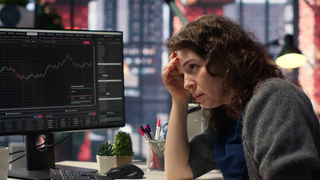 Donna preoccupata guarda un grafico finanziario su un monitor.