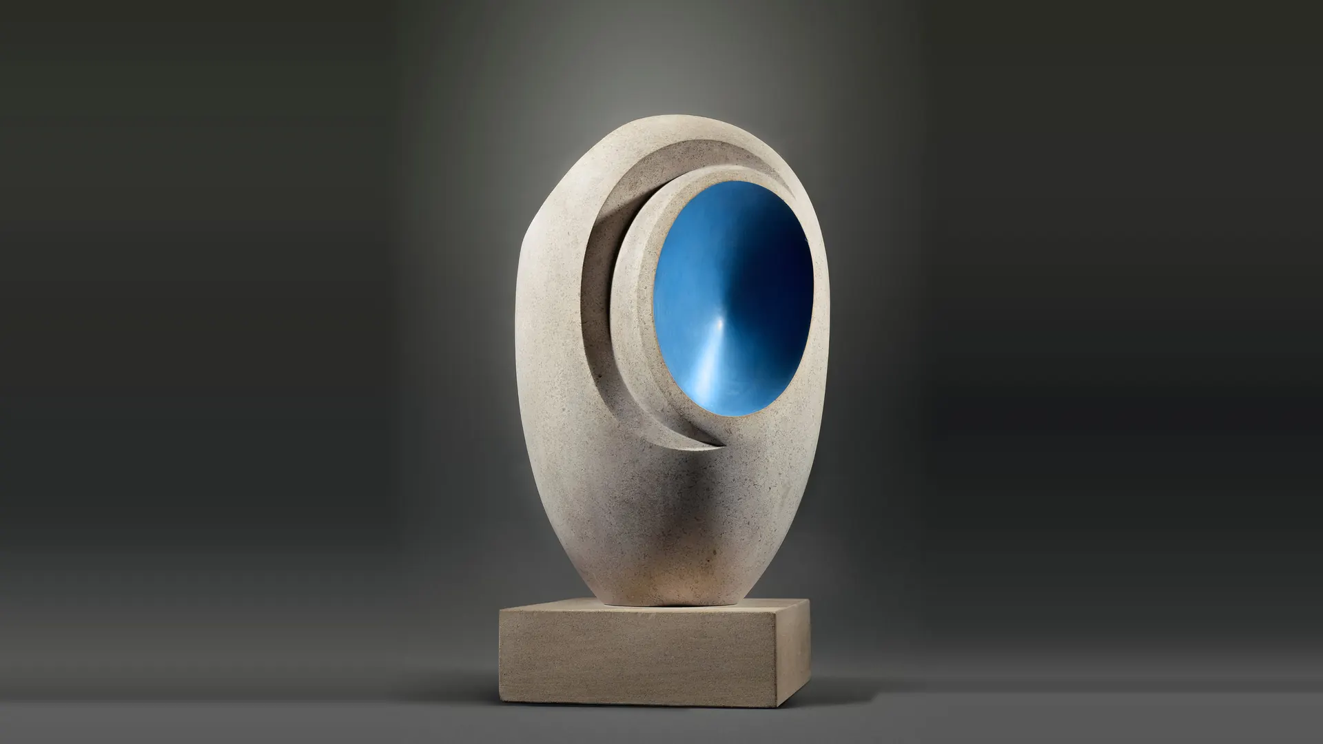 Scultura astratta in pietra chiara con cavità interna blu metallizzato, su base squadrata.