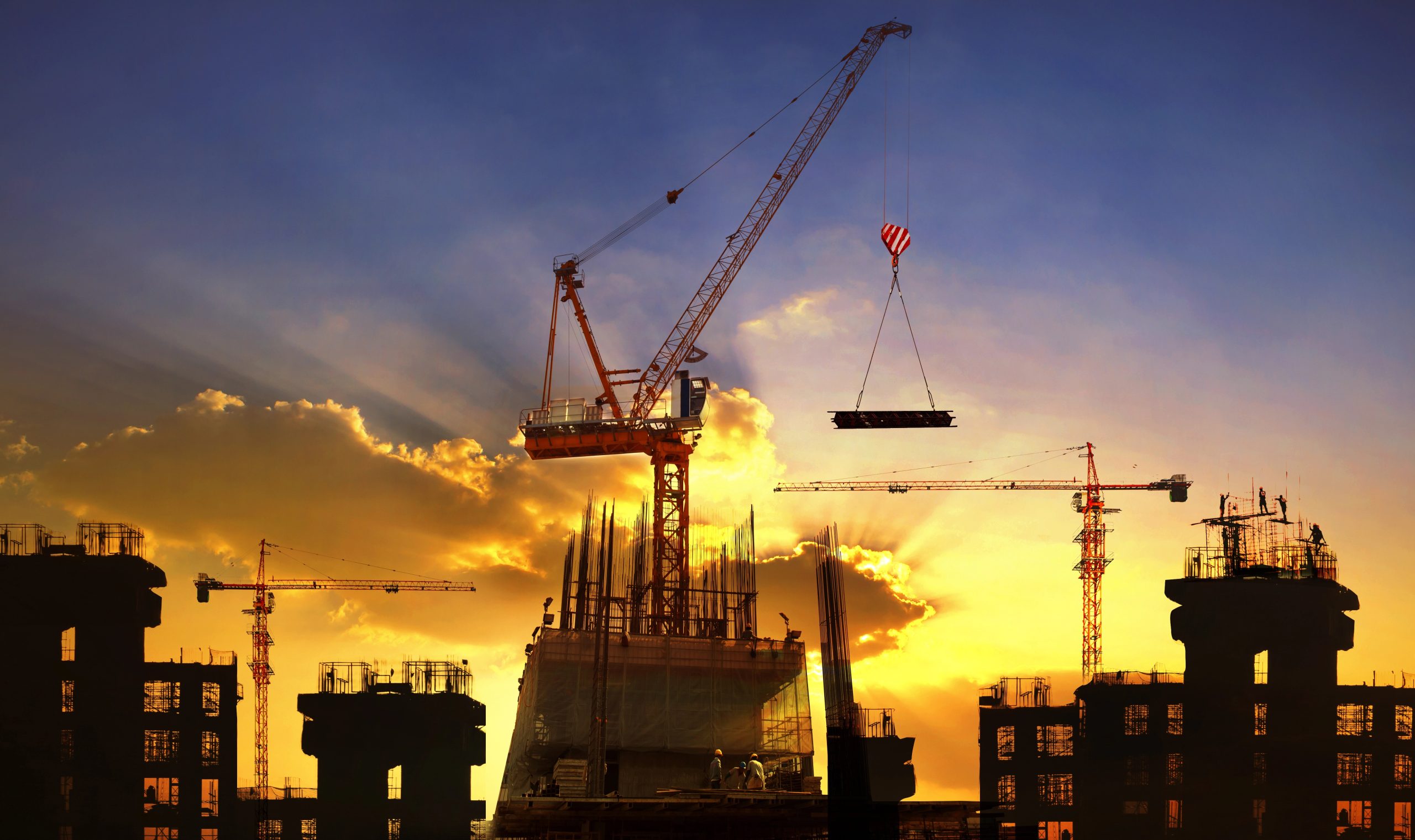 Gru gru e edifici in costruzione contro un tramonto dorato con nuvole drammatiche.