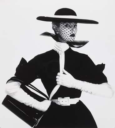 Modella con cappello a tesa larga, velo, guanti lunghi bianchi e borsa nera.