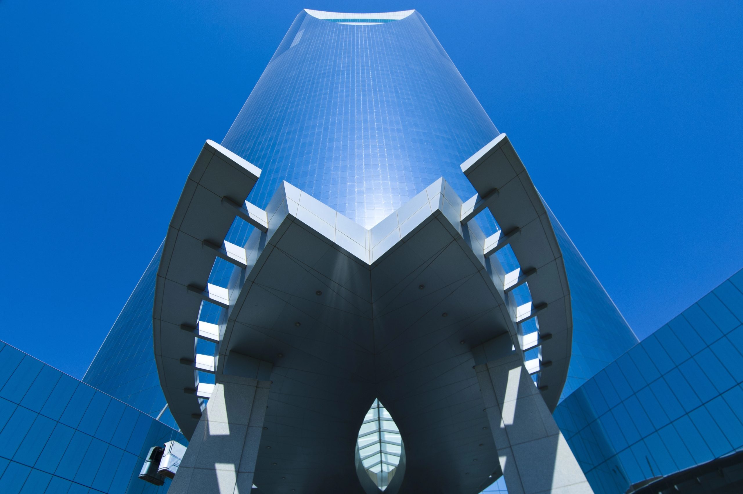 Edificio moderno con facciata in vetro blu, forme geometriche e cielo limpido.