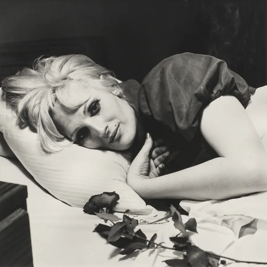 Donna bionda sdraiata su un letto, con rose rosse e un biglietto.