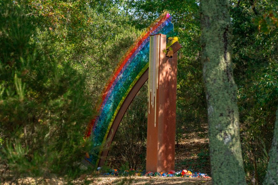 Scultura con arcobaleno di vetro colorato e pilastro arrugginito in un bosco.