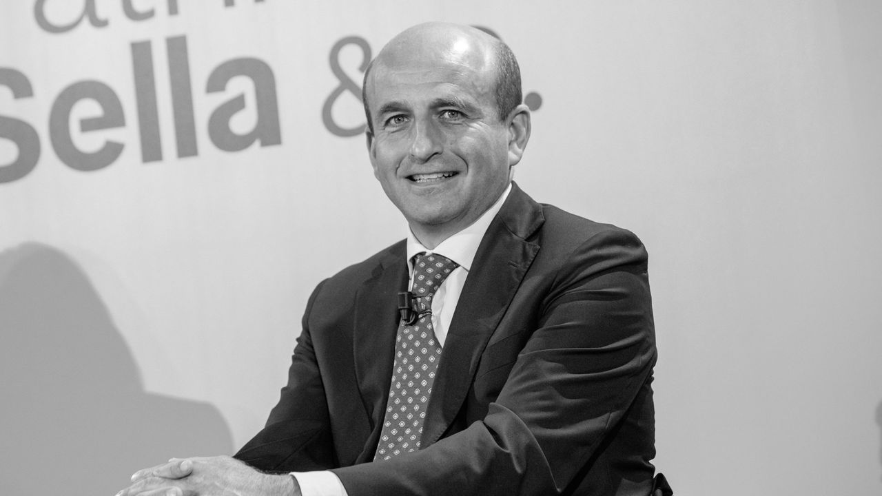 Uomo sorridente in giacca e cravatta, con logo "Sella &" sullo sfondo.