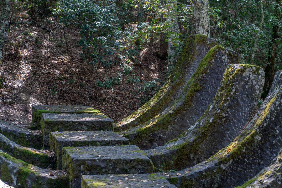 Antiche pietre ricoperte di muschio formano una scala e una struttura curva in un bosco.