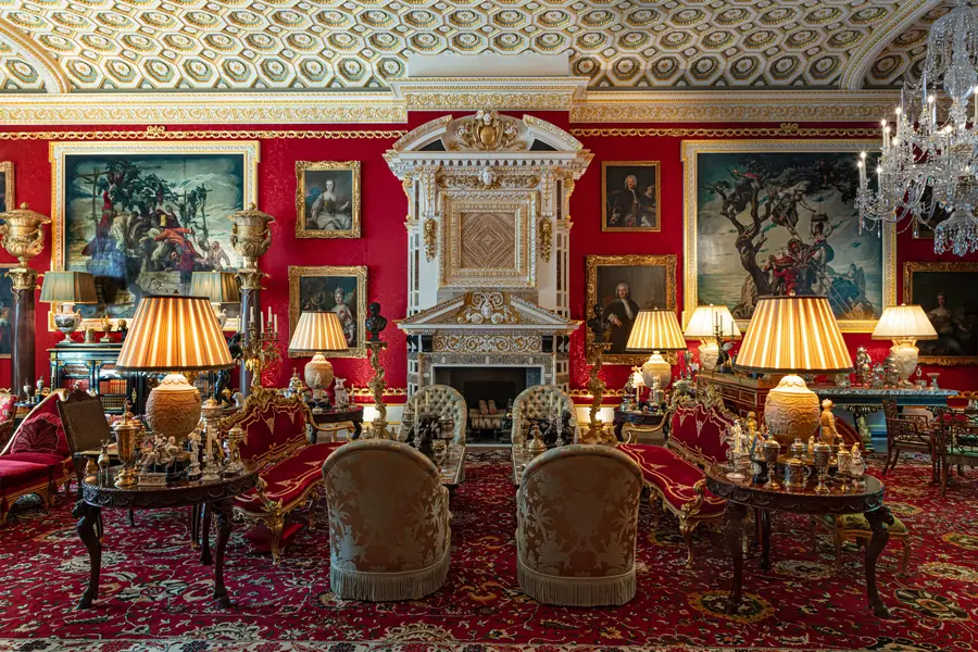 Salone rosso sontuoso con tappeto persiano, mobili dorati, dipinti e lampade.