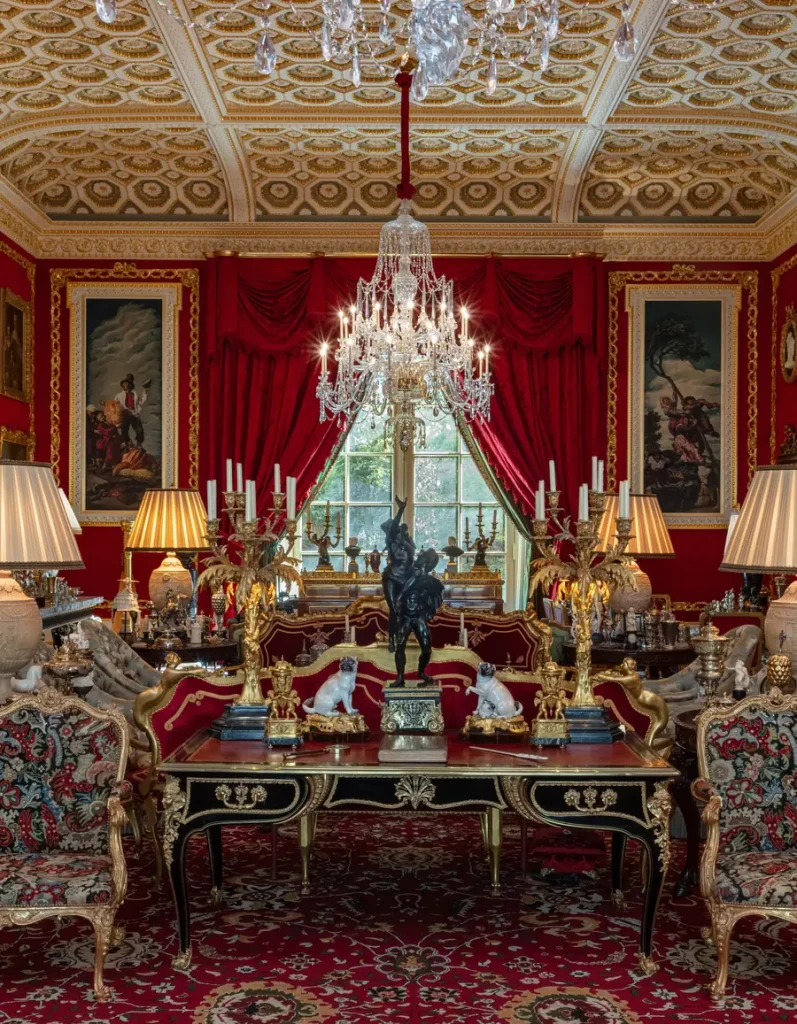Salone lussuoso con tappeto rosso, mobili dorati, dipinti e un grande lampadario.