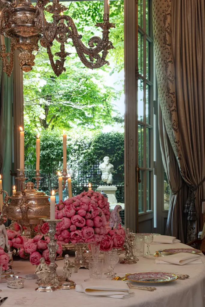 Tavola apparecchiata con fiori rosa, candele accese e un grande lampadario.