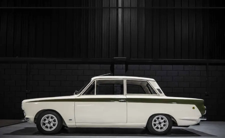 Auto d'epoca bianca con striscia verde, vista laterale, su sfondo scuro.